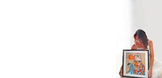 Mariló Nieto sola, sobre un fondo blanco, con vestido blanco, sentada en el suelo  posando con su Obra Cargas, mientras la sujeta entre sus manos y la mira desde arriba con cariño